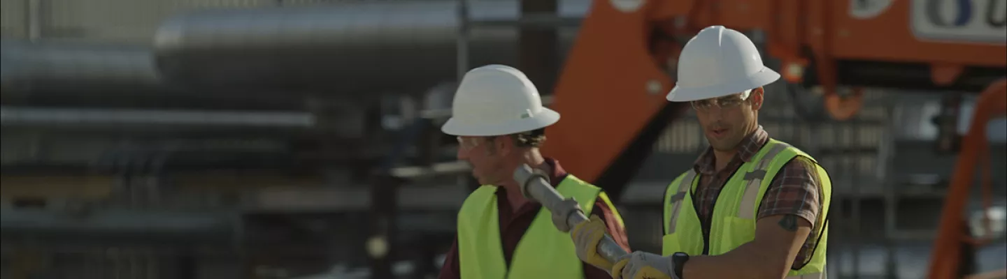 Two men on a construction site wearing hard hats, safety vests and safety glasses.
