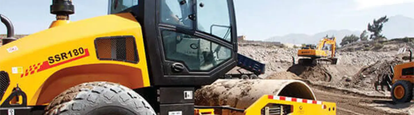 Men operating heavy machinery on a construction site, surrounded by safety barriers and wearing protective gear.