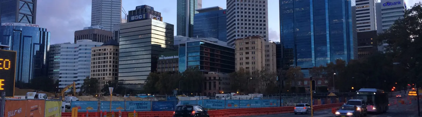 City road lined with orange safety barriers, demonstrating traffic control and pedestrian protection at a construction zone.