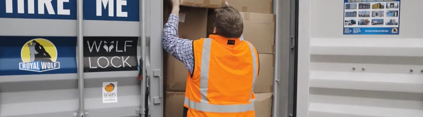 Worker in a high-visibility vest loading cardboard boxes into a storage container.