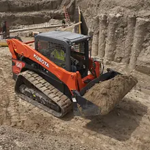 A track loader transporting sand across a construction site, supporting land grading and site preparation work.