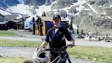 (Cassie Voysey) Person standing with a mountain bike in an alpine setting with snowy peaks in the background.
