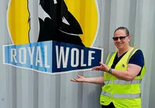 Woman standing and smiling in front of a company logo, representing professionalism and company pride.